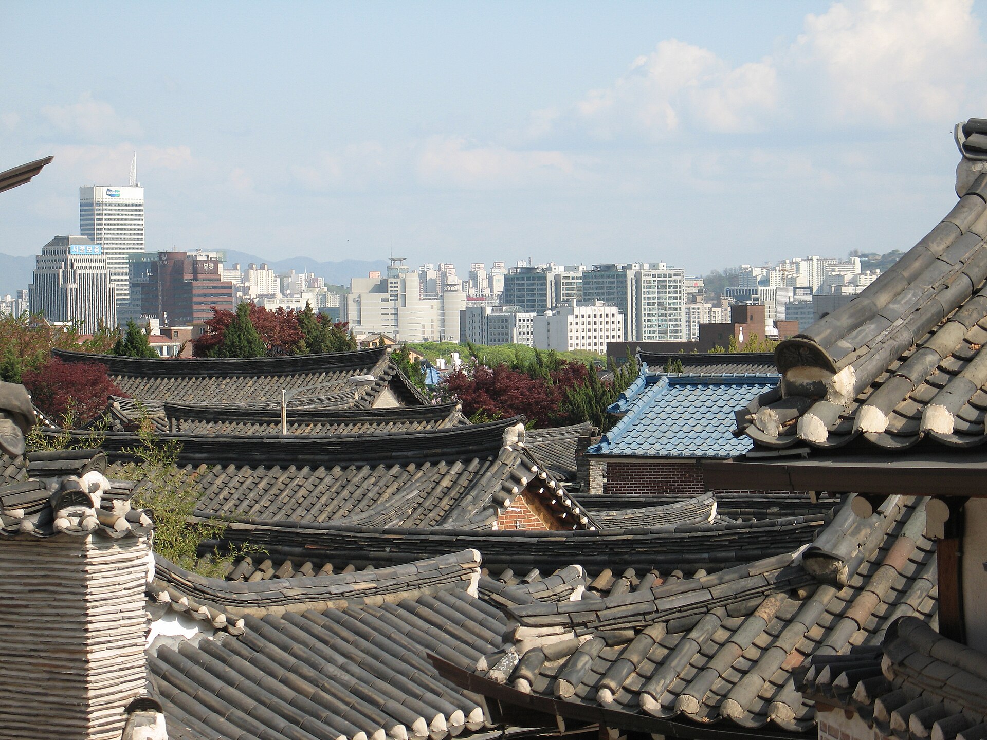 Tiled rooftops of traditional hanok houses in Bukchon Village with the Seoul skyline beyond